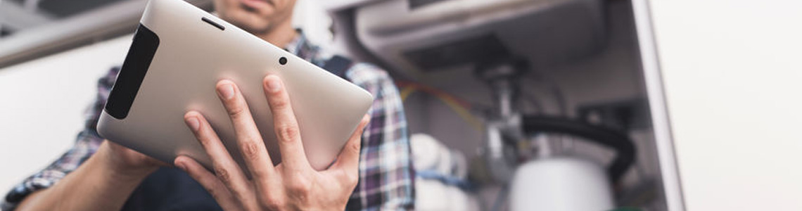 Person holding a tablet while inspecting or repairing plumbing under a sink.