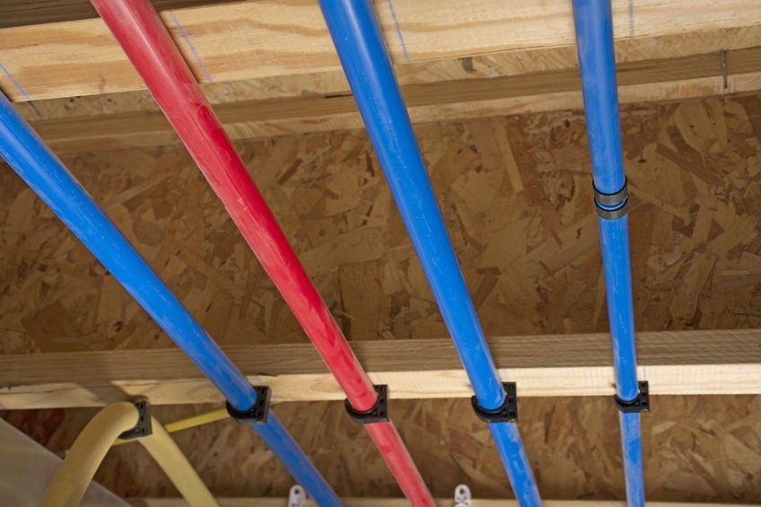 Close-up of red and blue water pipes installed along a wooden ceiling frame in a building under construction.